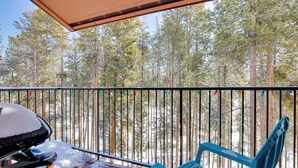 Un balcon avec un banc en bois et une chaise bleue, donnant sur une zone boisée.
