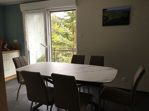 Zona pranzo con un tavolo grande e sei sedie, una finestra vista su piante, angolo cottura con elettrodomestico rosso e un quadro appeso al muro.
