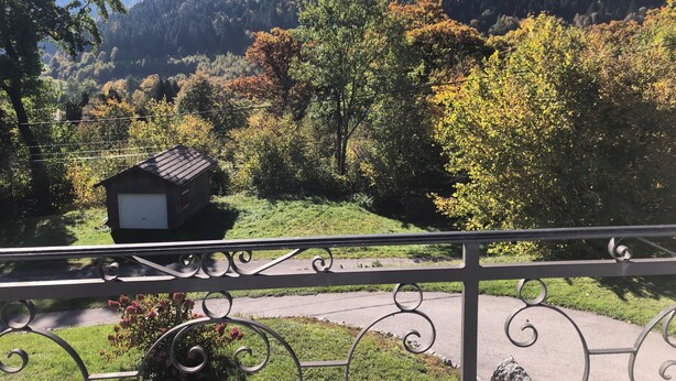 A scenic view of a mountainous area with autumn foliage, a small wooden cabin, and a metal railing in the foreground.