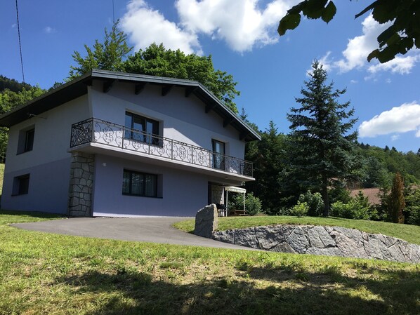 Una casa a due piani con un balcone, fondamenta in pietra e un muro di pietra davanti.
