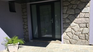 A modern building with a stone facade, a glass door, and a small planter with greenery.