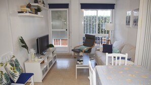Una sala de estar moderna y bien iluminada con televisor de pantalla plana, asientos cómodos, un sofá y una mesa de comedor.