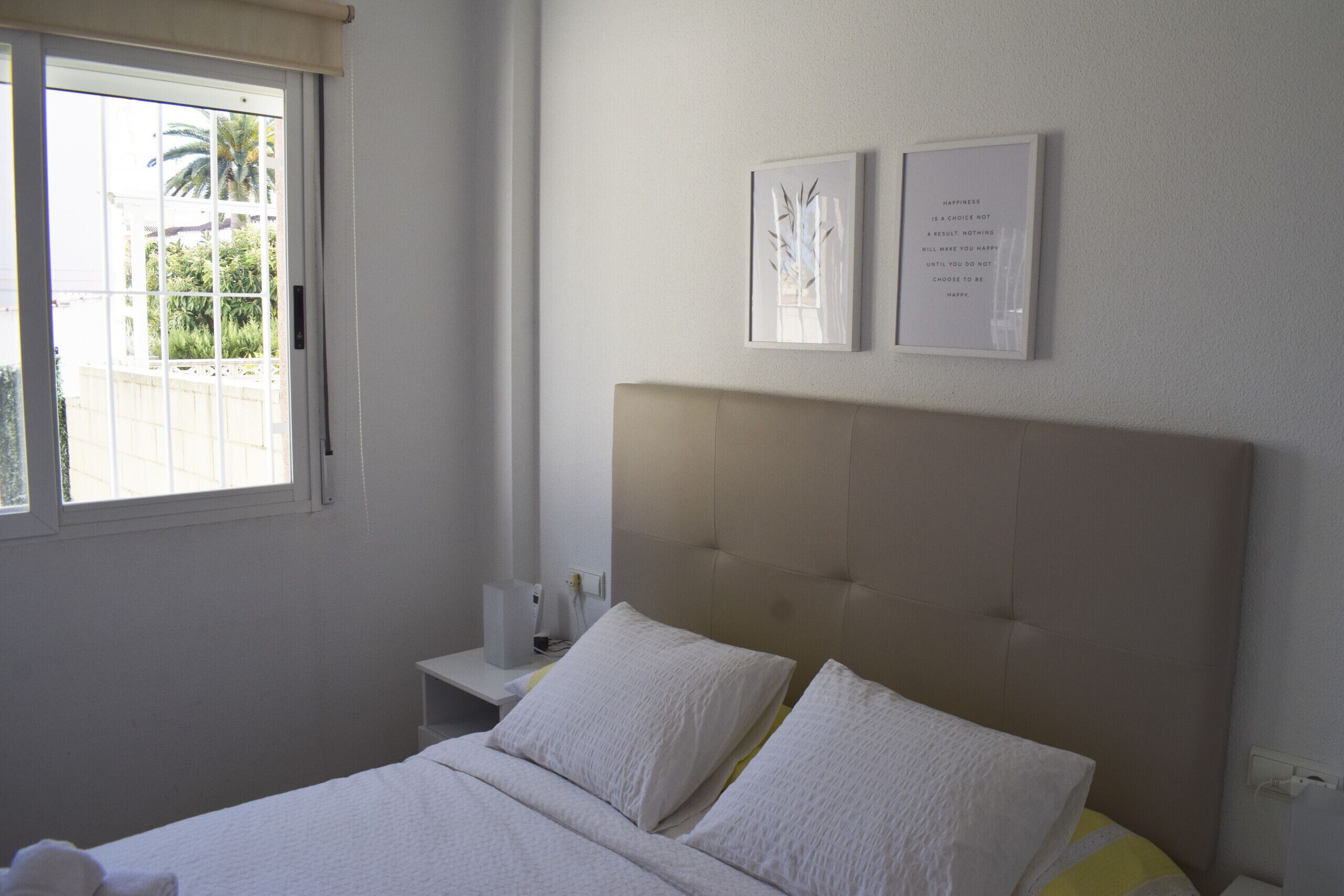 A bedroom with a bed, a nightstand, a window, and two framed pictures on the wall.