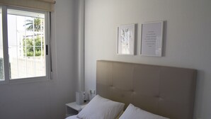 Un dormitorio con una cama, una mesita de noche, una ventana y dos cuadros en la pared.