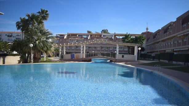 Una piscina con suelo de baldosas, rodeada de edificios y palmeras.