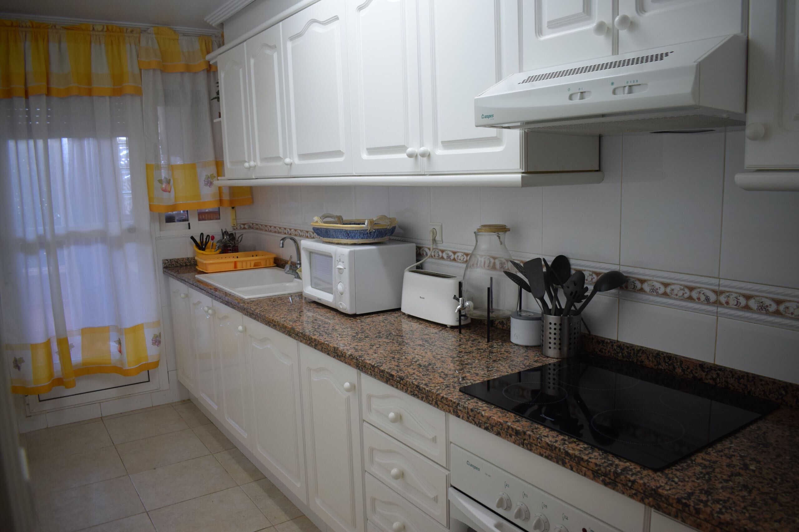 A kitchen with white cabinets, a granite countertop, a toaster, a kettle, and a sink.