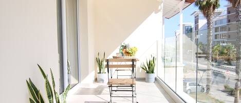 Un balcón con una mesa, plantas en macetas y vista a la calle.