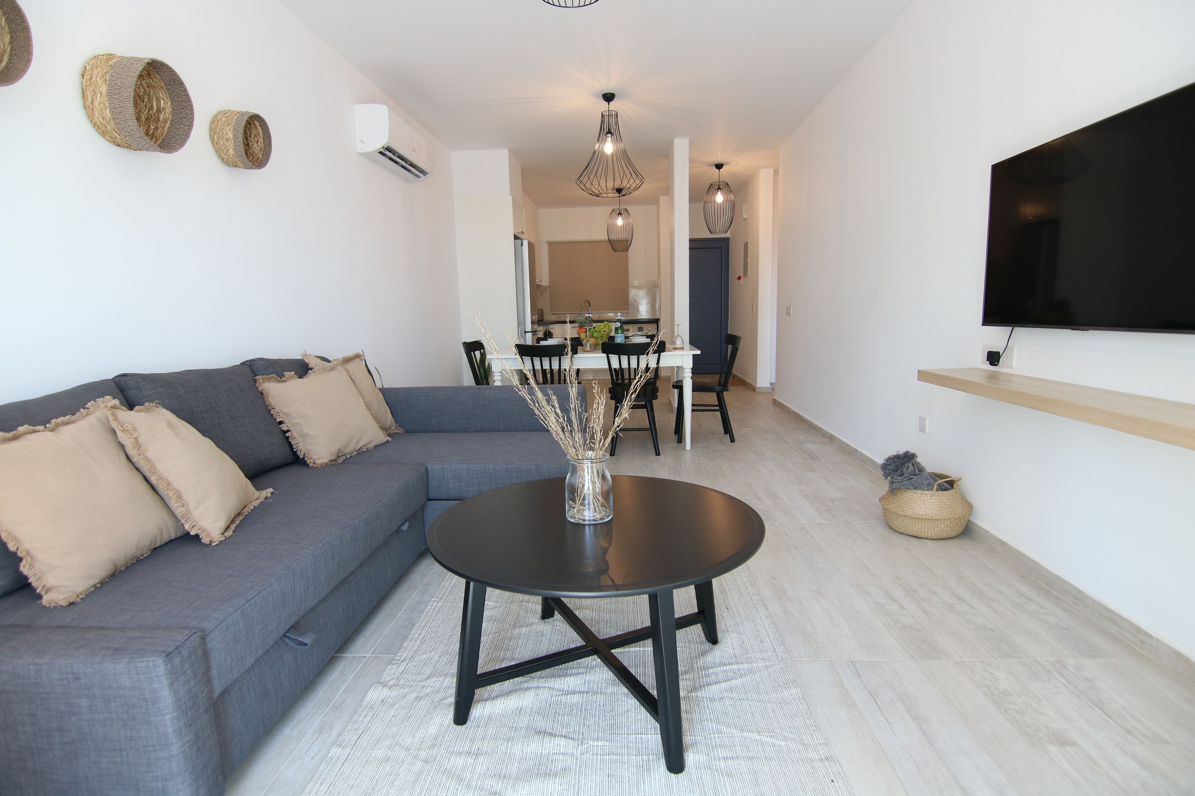 Una sala de estar moderna con un sofá gris, una mesa de centro redonda y una zona de comedor con una mesa y sillas blancas.