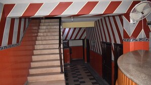 A staircase leading to a lower level with a checkered floor, red and white striped walls, and a fan mounted on the wall. - Hotel Royal Lodge (Islamabad)