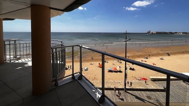 A beach view from a balcony with a clear sky, sandy beach, and a pier in the distance. - 2-star apartment with balcony-terrace, 1 bedroom, parking, close to the sea (Les Sables-d'Olonne)