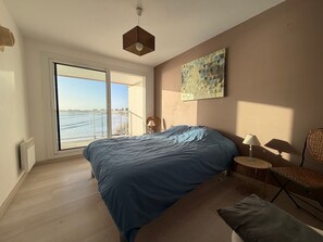 A bedroom with a large bed, a view of the sea, a painting on the wall, and a ceiling light. - 2-star apartment with balcony-terrace, 1 bedroom, parking, close to the sea (Les Sables-d'Olonne)