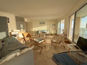 A spacious living area with a sofa, wicker chairs, a dining table, and a television. - 2-star apartment with balcony-terrace, 1 bedroom, parking, close to the sea (Les Sables-d'Olonne)
