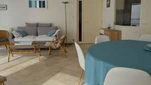A modern living room with a sofa, chairs, a dining table, and a large window. - 2-star apartment with balcony-terrace, 1 bedroom, parking, close to the sea (Les Sables-d'Olonne)