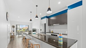 Una cucina moderna con isola centrale, sgabelli da bar, luci a sospensione e vista sull'area living.