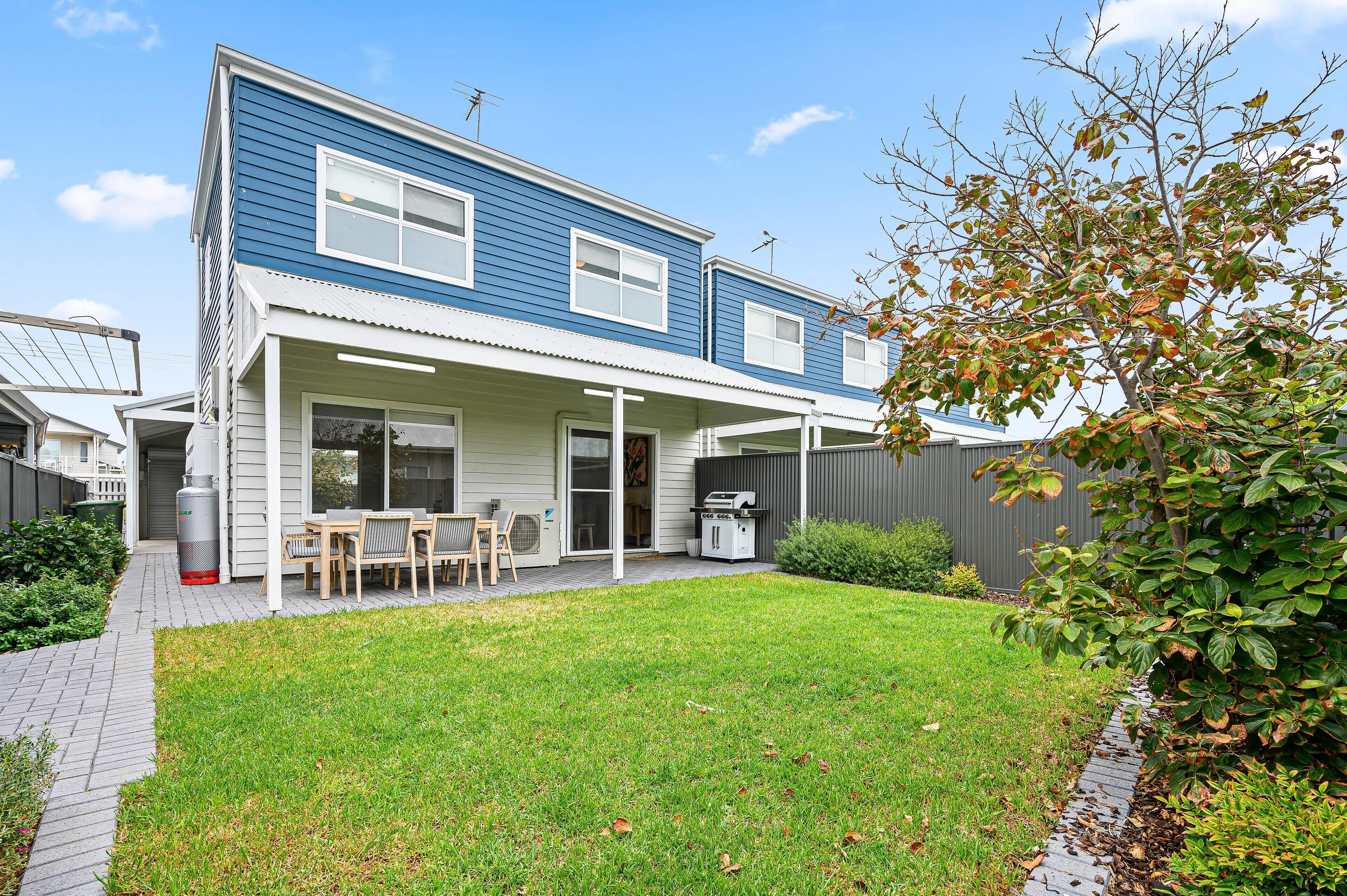 A two-story house with a covered patio, a lawn, and a wooden deck.