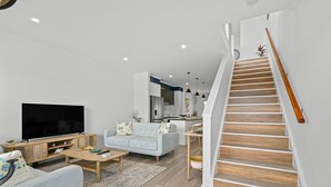 Un soggiorno moderno con una TV a schermo piatto, un divano azzurro chiaro e un tavolino in legno. Una scala con ringhiera in legno conduce a un livello superiore.