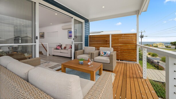 Una zona relax esterna moderna con un pavimento in legno, mobili in vimini e una porta vetrata che dà su un ambiente interno.