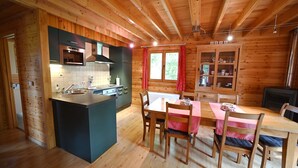 L’intérieur d’un chalet en bois comprend une cuisine, un coin repas et une fenêtre avec des rideaux.
