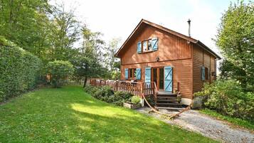 A wooden cabin with a porch, surrounded by lush greenery.