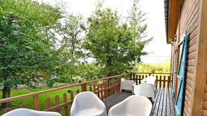 Une terrasse en bois avec des chaises et une table en plastique blanc, donnant sur un espace verdoyant avec des arbres.