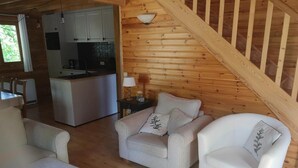 L’intérieur d’un chalet accueillant, avec un escalier en bois, un coin repas et un salon comprenant deux canapés et une lampe.