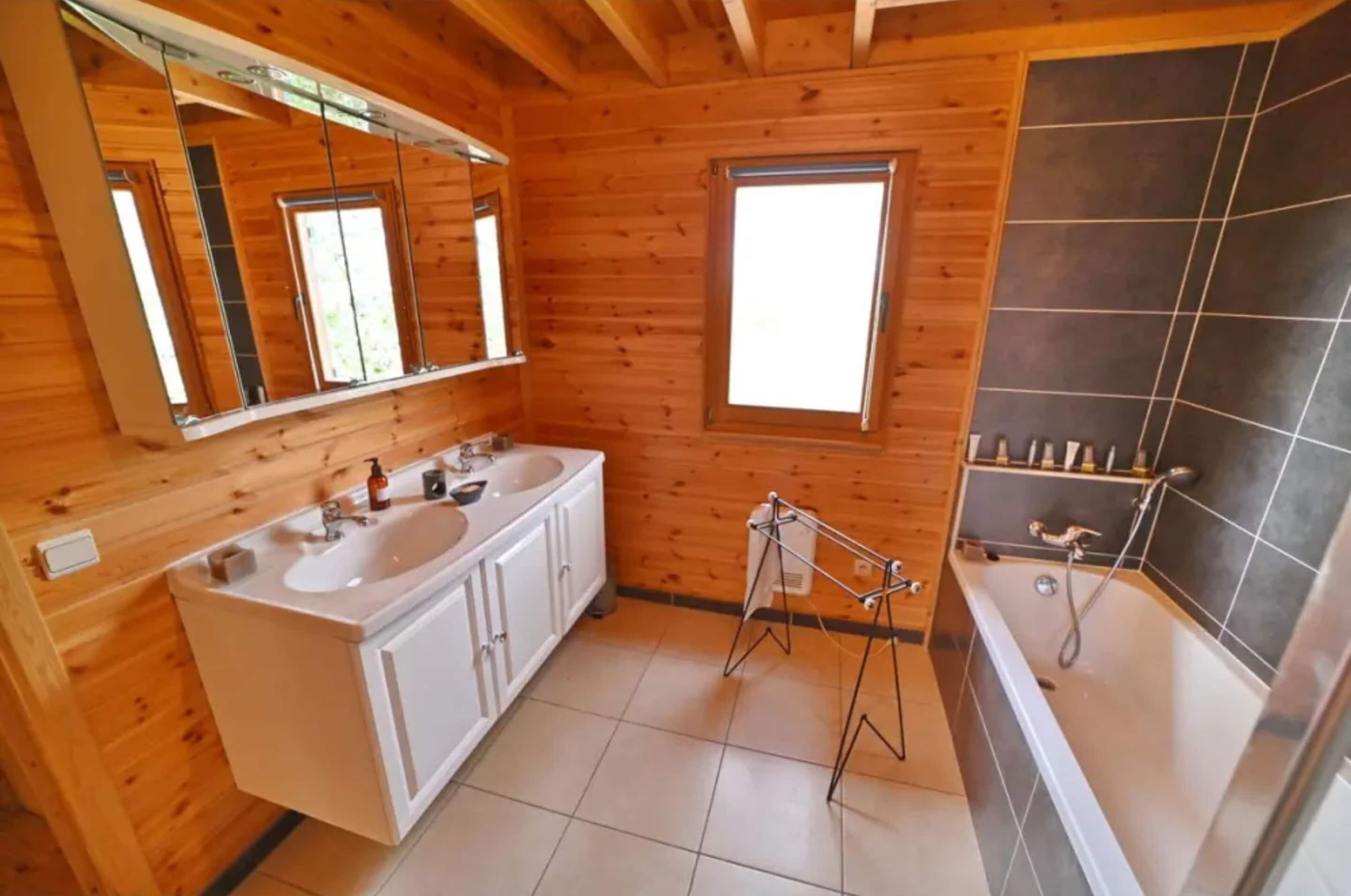 A wooden cabin bathroom with two sinks, a large mirror, a bathtub, and a window.