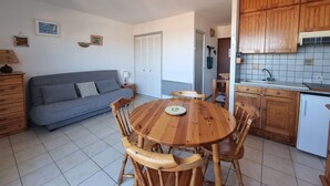 Un espacio habitable compacto con sofá, mesa de comedor, sillas y una zona de cocina con armarios de madera y salpicadero de azulejos.