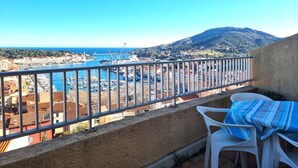 Un balcón con vistas a un puerto deportivo, barcos y una montaña al fondo.