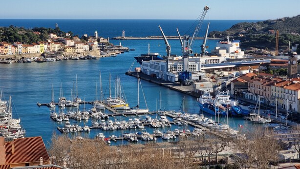 Un puerto con numerosos barcos amarrados, una grúa y edificios a lo largo del muelle.