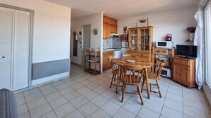 Cocina compacta con armarios de madera, una mesa de comedor con sillas, un microondas y un televisor.