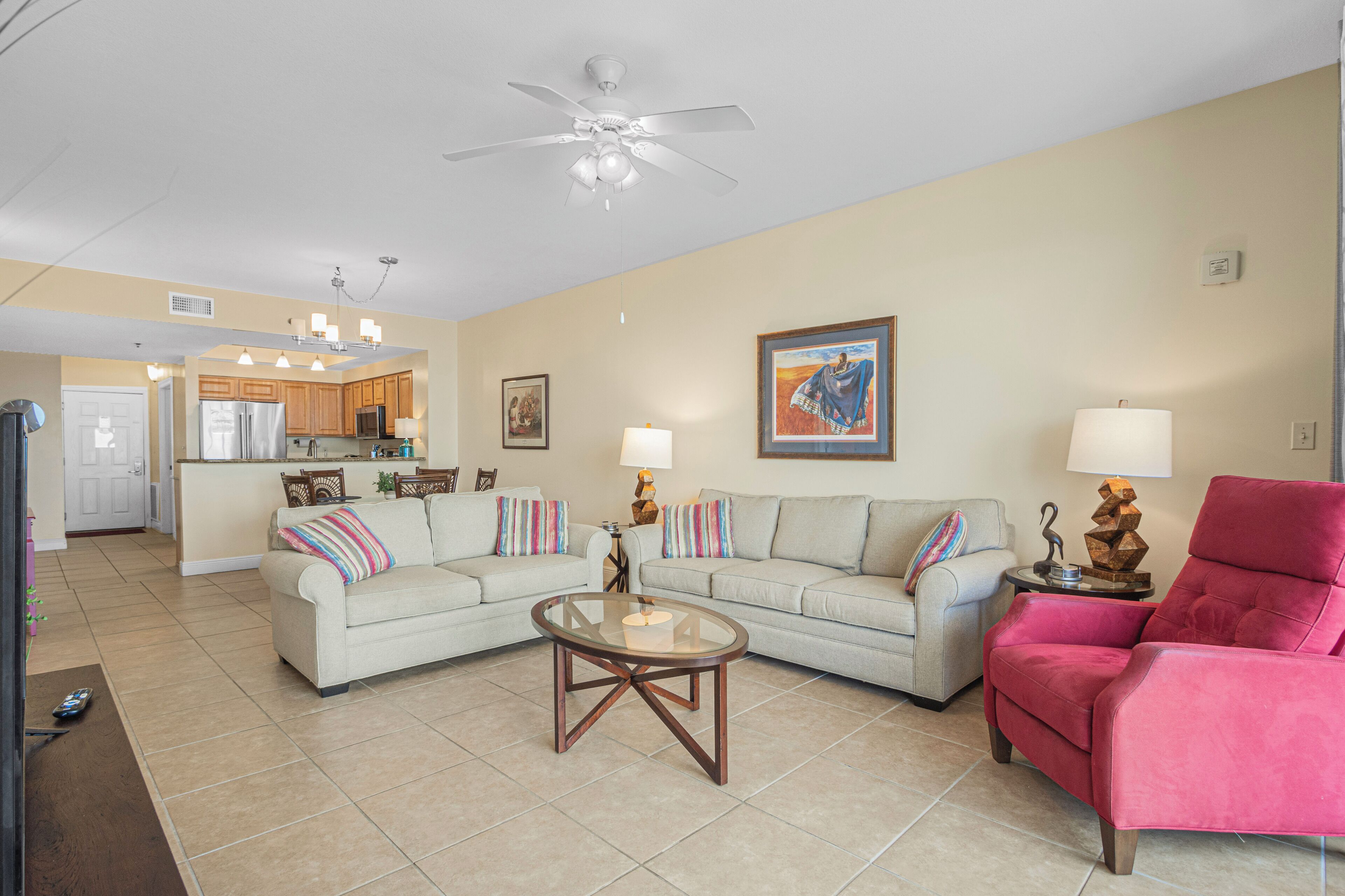 A living room with two sofas, a coffee table, a red armchair, and a kitchen in the background.