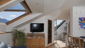 A modern living room with a TV, wooden furniture, a plant, and a view of the outdoors. - Above the rooftops of Lana - Blue apartment with terrace and sauna - viaDolceVita (Lana)