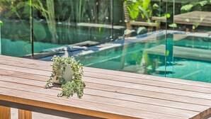 A wooden deck with a potted plant and a glass railing overlooking a pool.