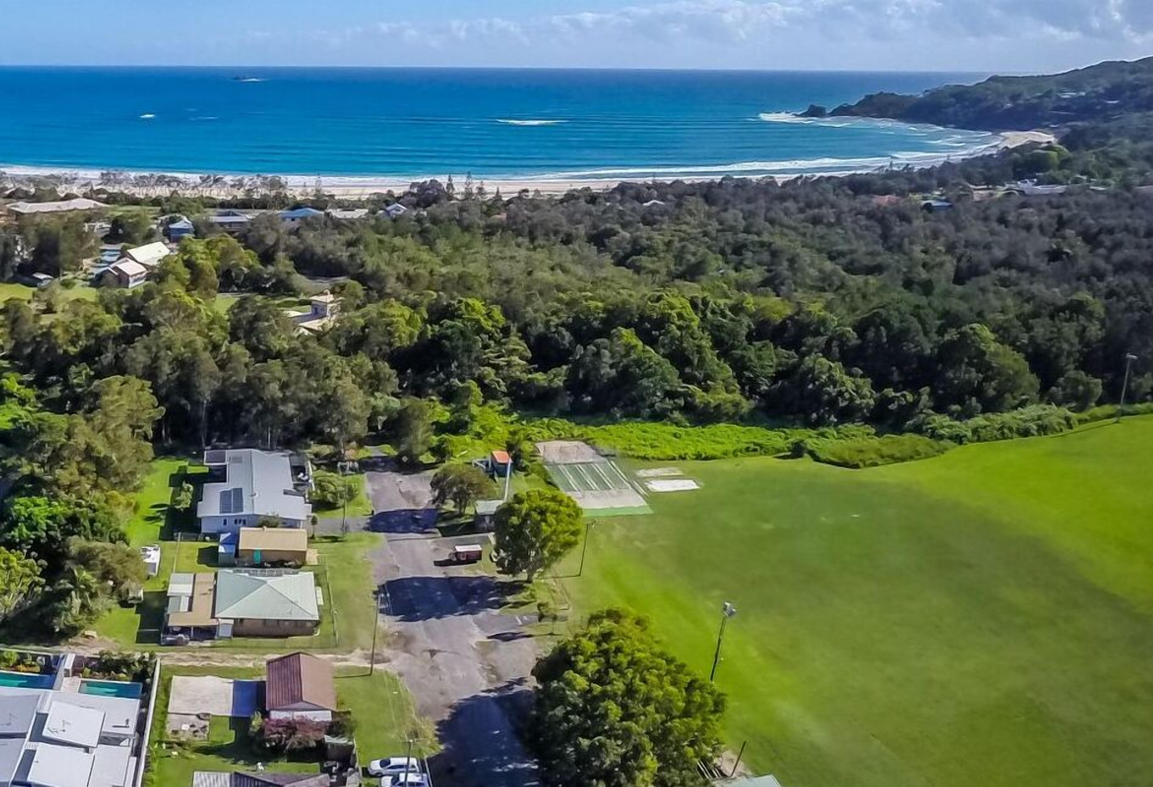 An aerial view of a coastal area with a beach, dense forest, and residential buildings.
