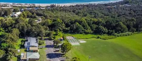 An aerial view of a coastal area with a beach, dense forest, and residential buildings.