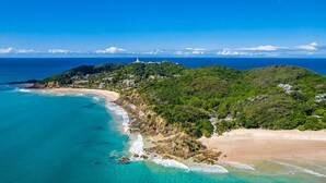 A coastal area with a beach, a lighthouse, and a hill with buildings.
