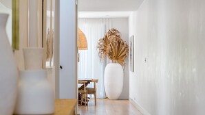 A hallway with a large white vase, a wooden table, and a chair.