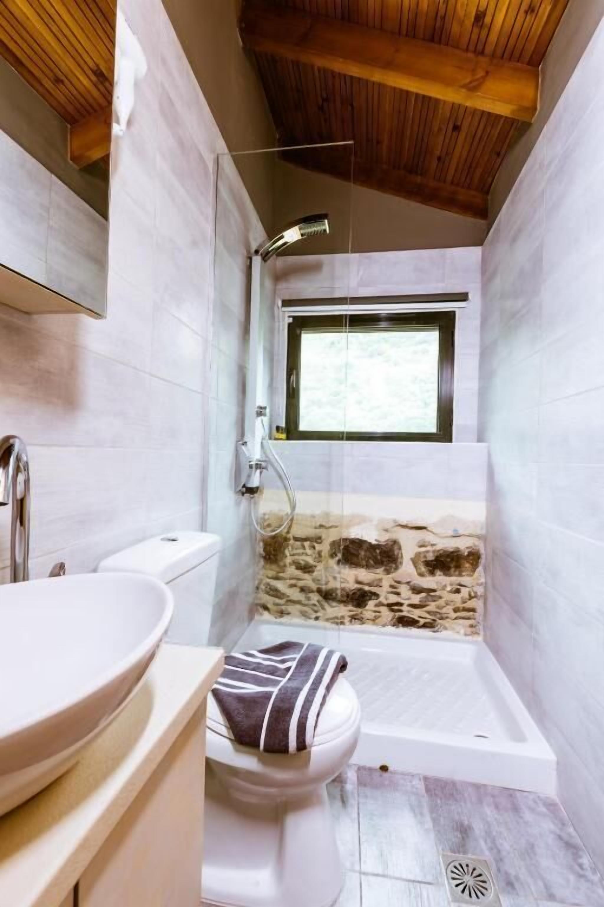 A bathroom with a stone wall, a window, a bathtub, and a toilet.