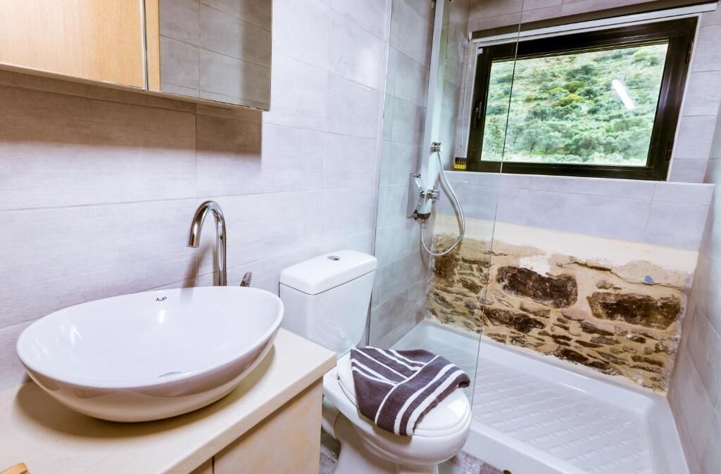 Un baño con lavamanos blanco, inodoro y ducha con pared de piedra.