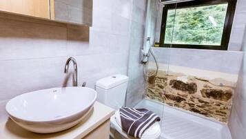 Un baño con lavamanos blanco, inodoro y ducha con pared de piedra.