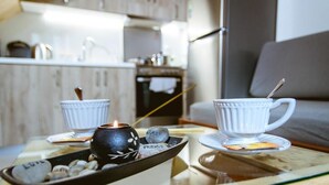 A cozy living area with a glass-top table holding two white cups and a candle, and a tray with stones and a name tag. - Ellafos Traditional Living (Kissamos)