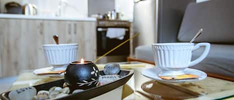 Un espacio de sala acogedor con una mesa de vidrio que sostiene dos tazas blancas y una vela, y una bandeja con piedras y una identificación.