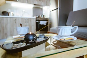 Un espacio de sala acogedor con una mesa de vidrio que sostiene dos tazas blancas y una vela, y una bandeja con piedras y una identificación.