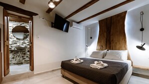 A bedroom with a bed, a TV, a wooden headboard, and a stone wall. - Ellafos Traditional Living (Kissamos)