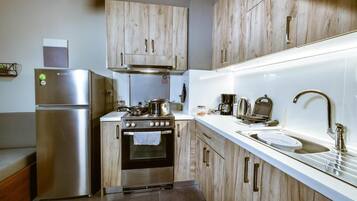 A compact kitchen with a stainless steel refrigerator, an oven, a sink, and wooden cabinets.
