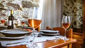 A dining table set with plates, cutlery, and wine glasses, with a stone wall background. - Ellafos Traditional Living (Kissamos)