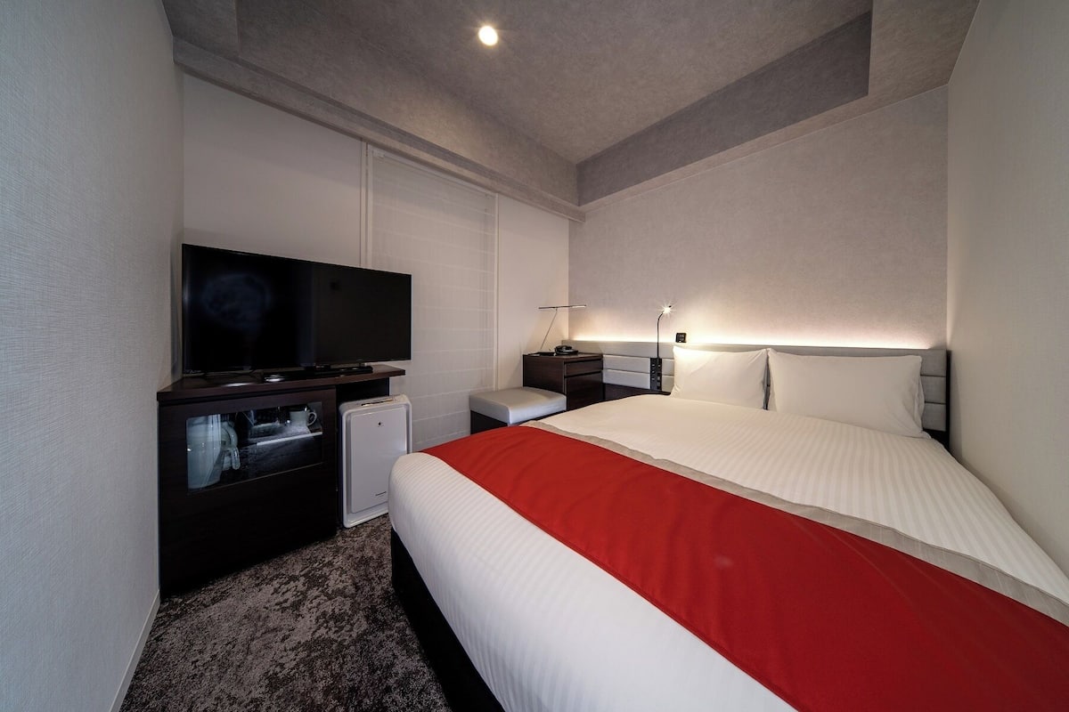 Een hotelkamer met een bed, een televisie, een bureau met een lamp en een kleine koelkast.