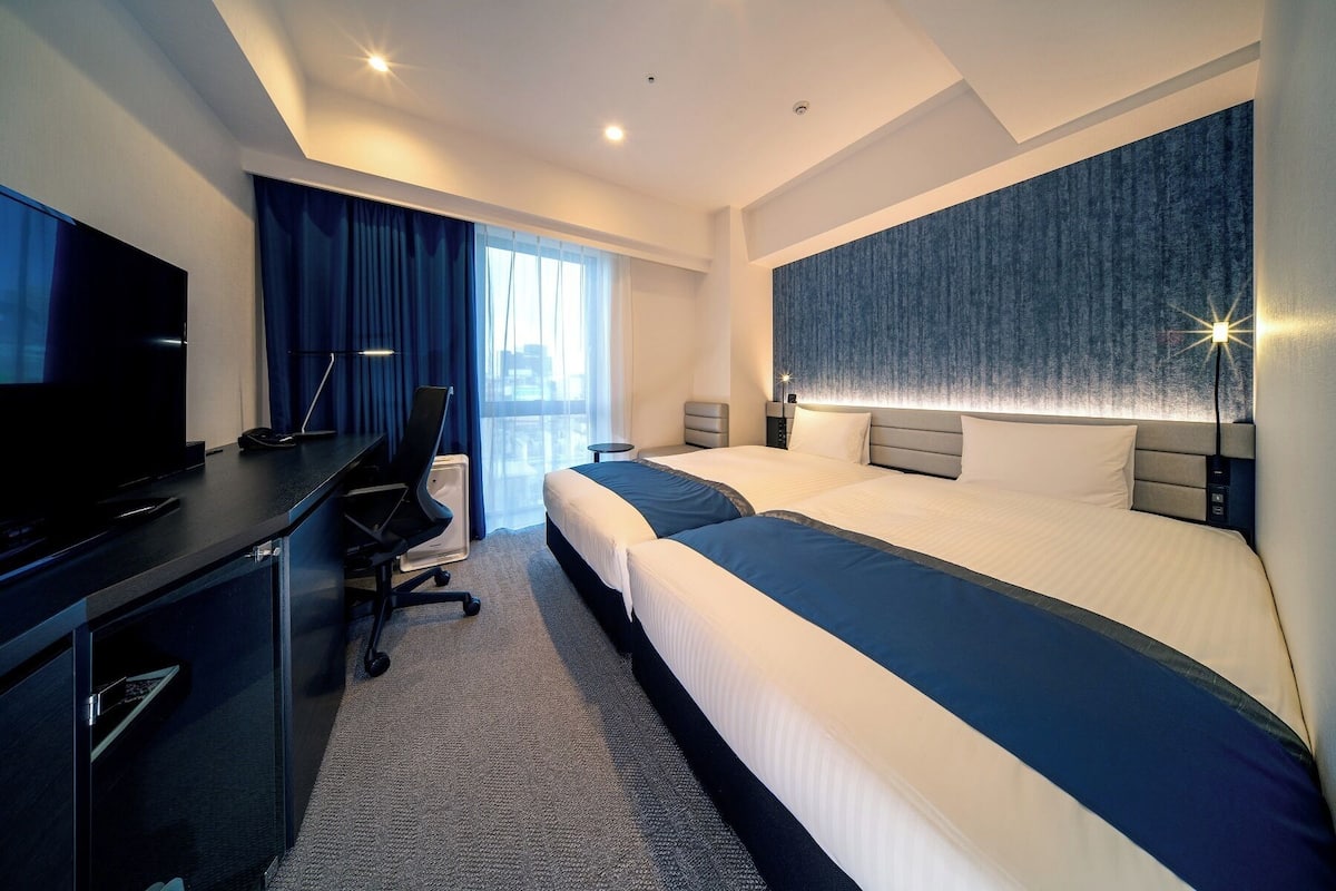 Una habitación de hotel moderna con una cama grande, un escritorio con televisor de pantalla plana y una silla.