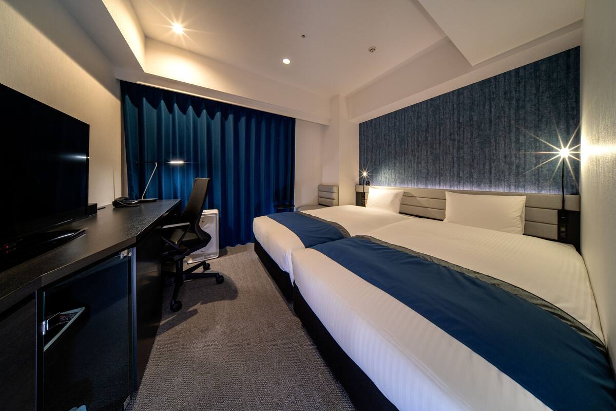 Een moderne hotelkamer met een groot bed, een bureau met een televisie en een blauw gordijn.
