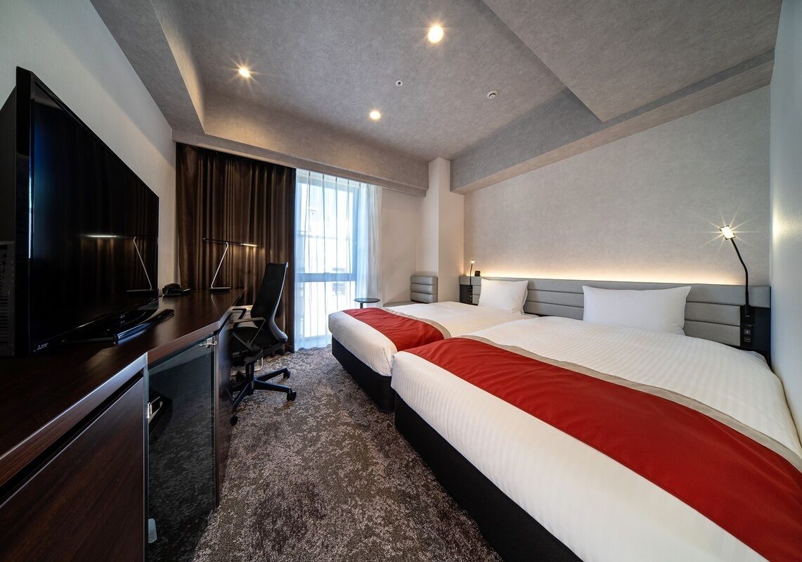 A hotel room with a bed, desk, TV, and a view of the outside.